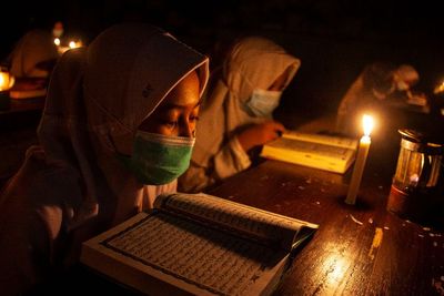 FOTO: Mengaji Al Quran Diterangi Cahaya Lilin